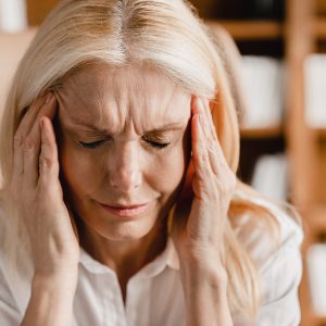 Caucasian mature middle-aged businesswoman rubbing her temples while suffering from headache, depression, overworked, migraine, coronavirus. Health problems at workplace